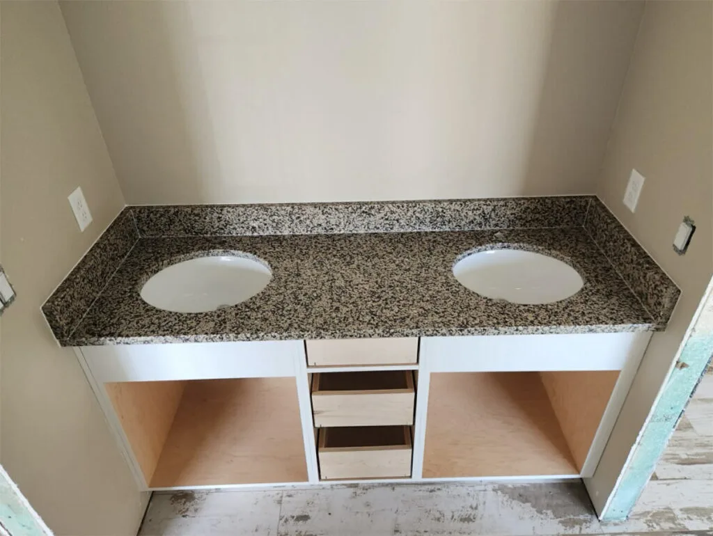 Granite bathroom countertop with two sinks and storage.