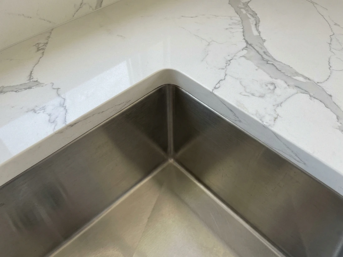 Undermount sink cutout in a quartz countertop showing a plain edge band around the bowl