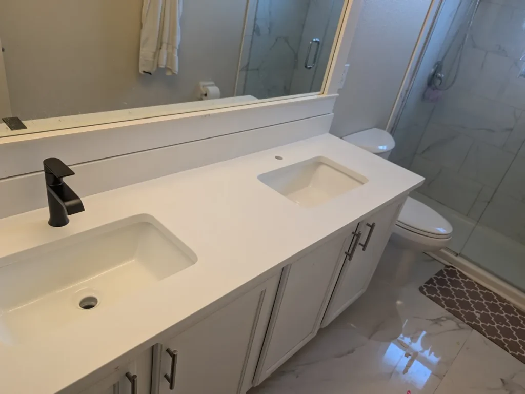 Same bathroom after EdStone installed Carrara Total White quartz with undermount sinks and a black faucet