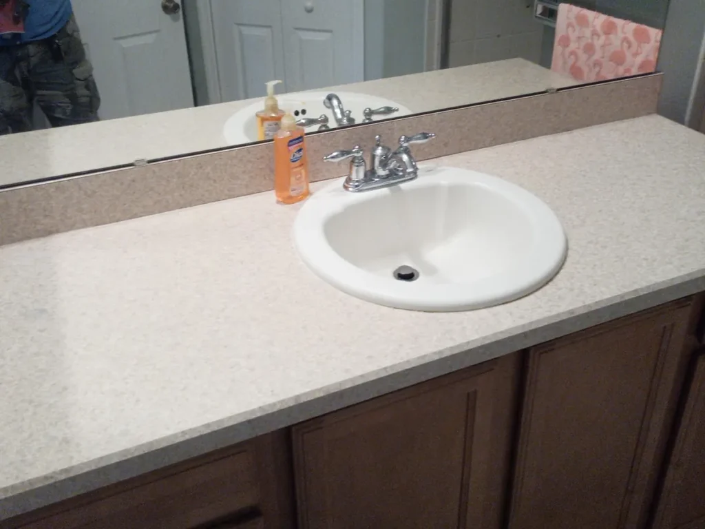 Bathroom before replacement, a dated countertop with a drop-in sink