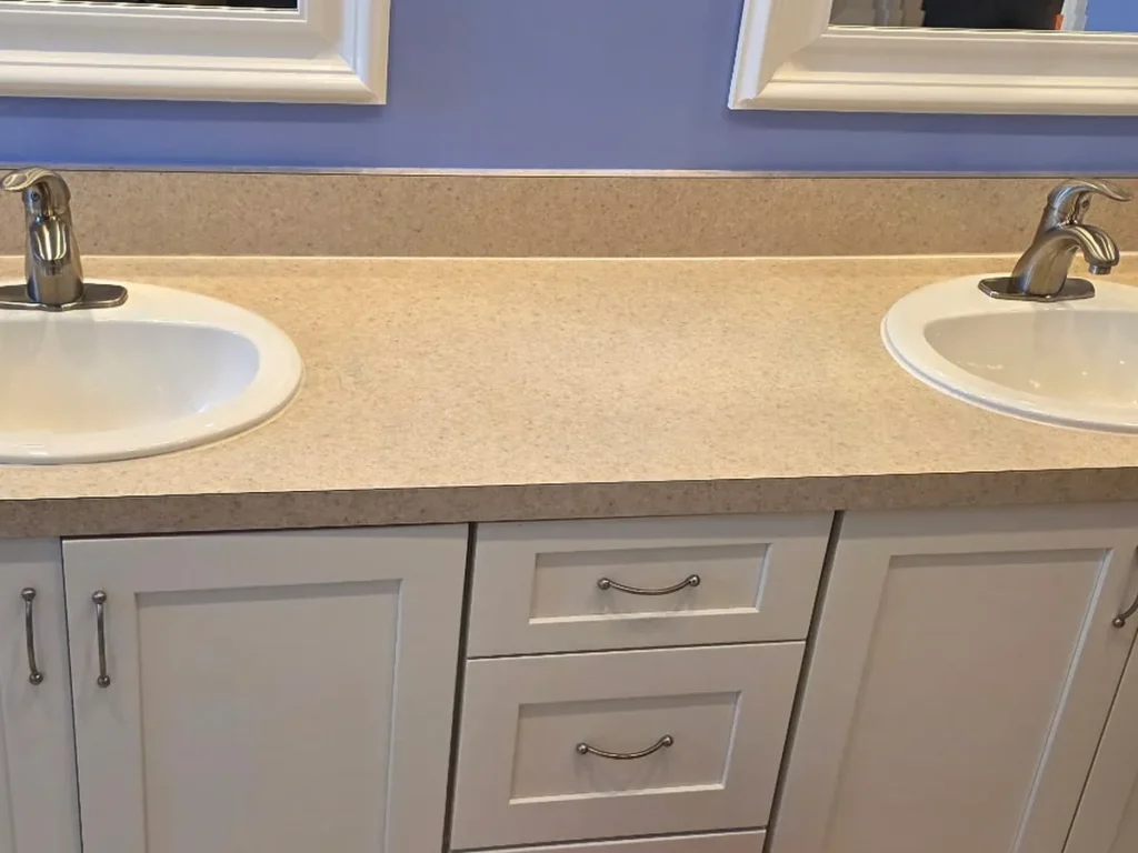 Double-sink bathroom before replacement, a dated countertop with drop-in sinks
