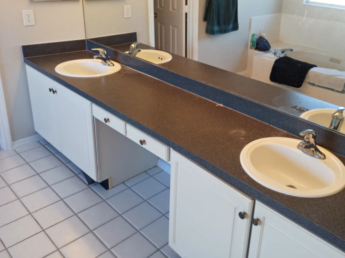 Dark laminate top on a white double vanity with two drop-in sinks and a makeup section