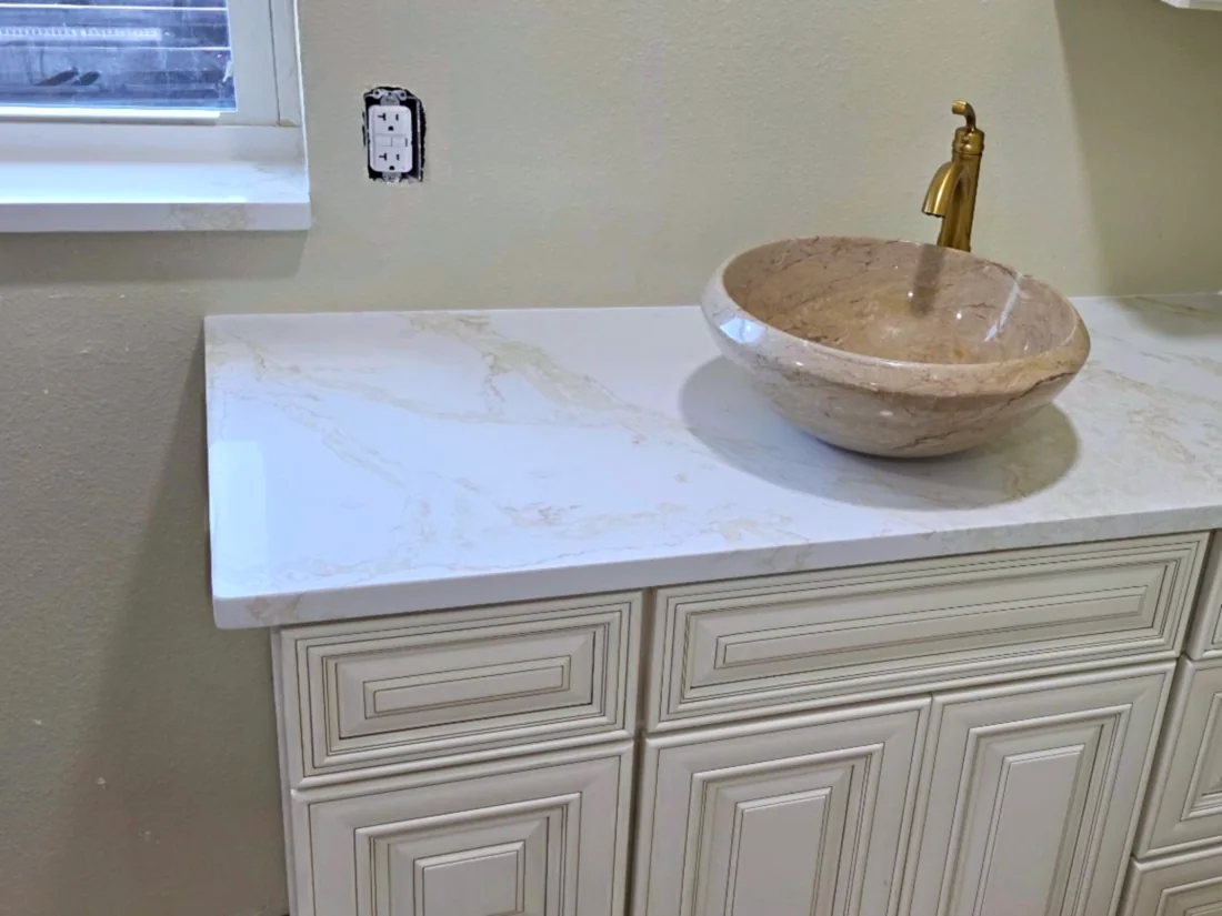 White quartz vanity top with gold veining, round beige stone vessel sink and brushed-gold faucet