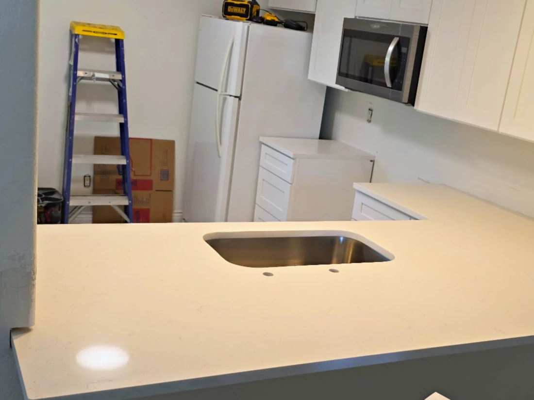 Warm white quartz L-shaped counter with undermount sink running through a kitchen wall opening