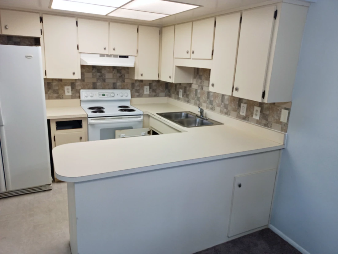 Older U-shaped kitchen with cream laminate countertops, rounded peninsula end and white electric range