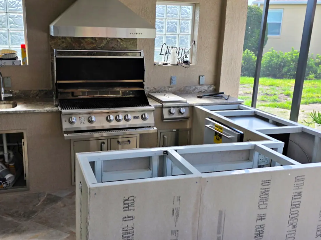 Outdoor kitchen island framed in metal studs and cement board next to a built-in grill on a screened lanai