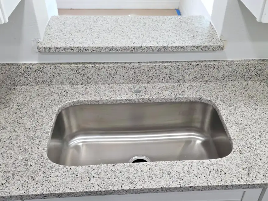 Speckled gray and white granite counter with undermount sink and matching granite ledge in wall opening